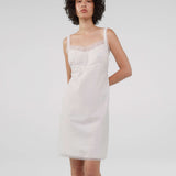 Woman wearing a white slip dress against a plain background