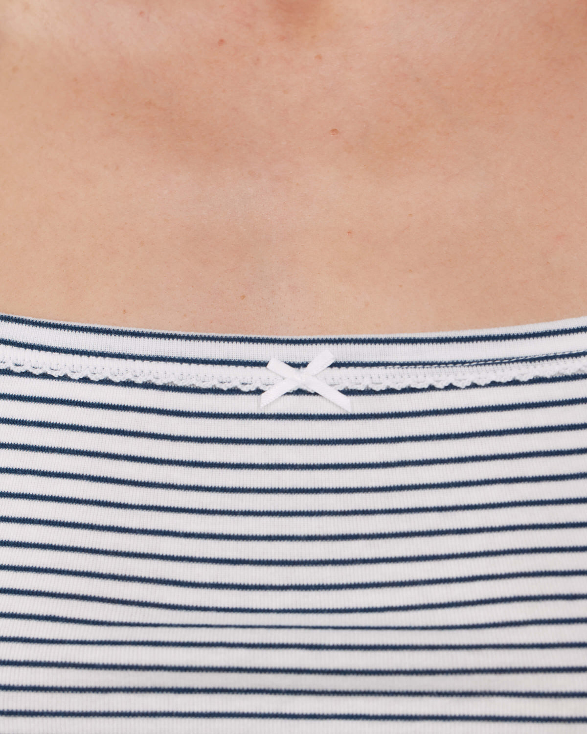 Close-up of a person wearing a white top with thin navy horizontal stripes and a small white bow at the neckline.