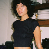 Woman wearing a black crop top in an indoor setting with shelves and plates in the background