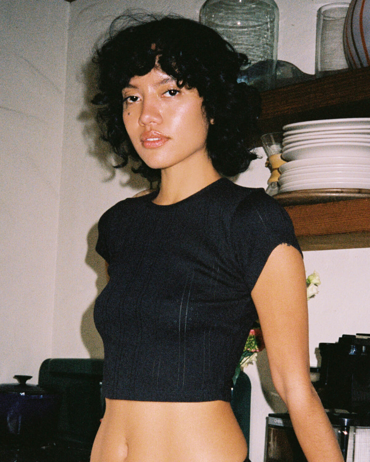 Woman wearing a black crop top in an indoor setting with shelves and plates in the background