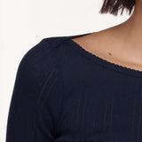 Close-up of a person wearing a dark navy textured knit top with a scalloped neckline, against a plain light background.