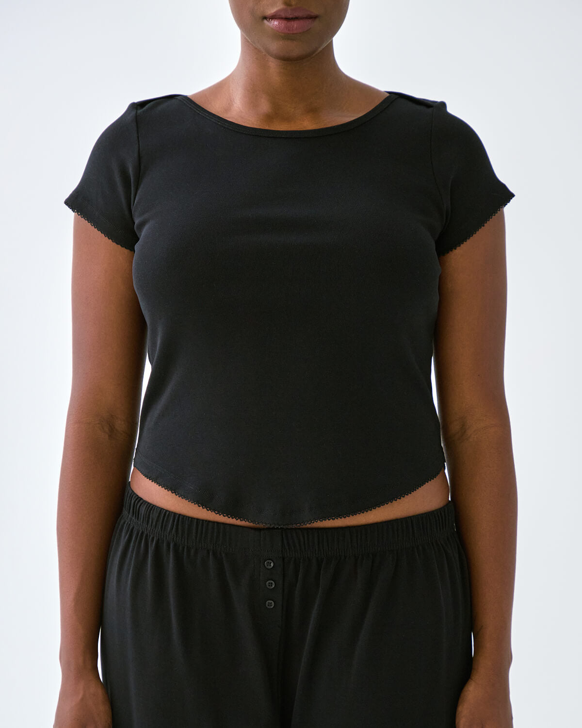 Person wearing a black crop top and black pants on a white background