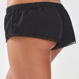Black lace-trimmed shorts worn by a person on a white background