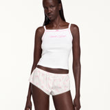 Woman wearing a white tank top with white shorts with a pink pattern and lace trim. 