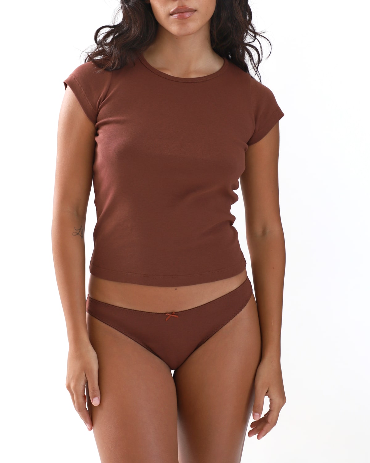 Woman wearing a brown cap sleeve top and brown brief on a white background
