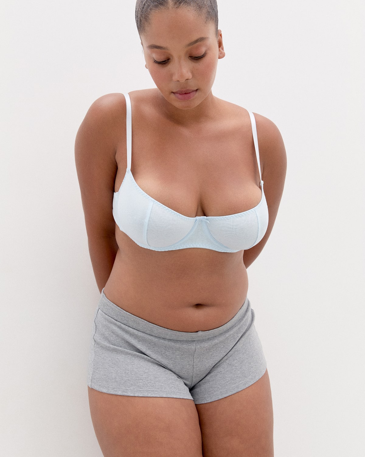 Woman wearing a light blue bra and gray shorts against a white background