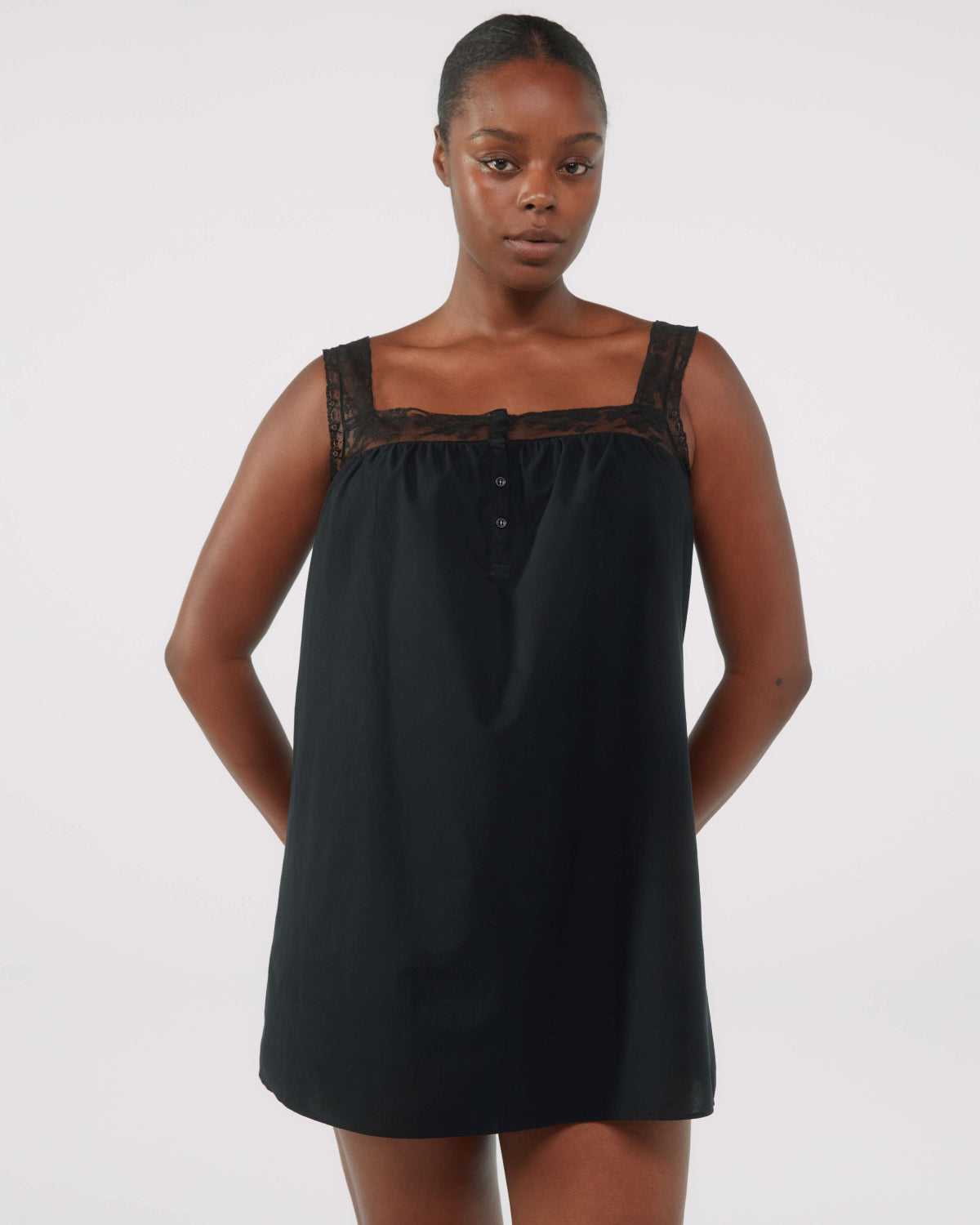 Woman wearing a black sleeveless dress with lace details on a white background