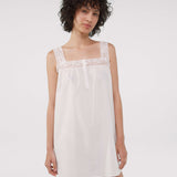 Woman wearing a white dress with lace details on a plain background