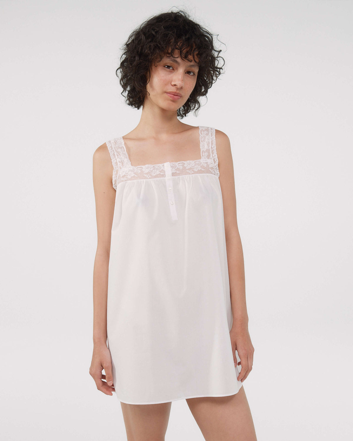 Woman wearing a white dress with lace details on a plain background