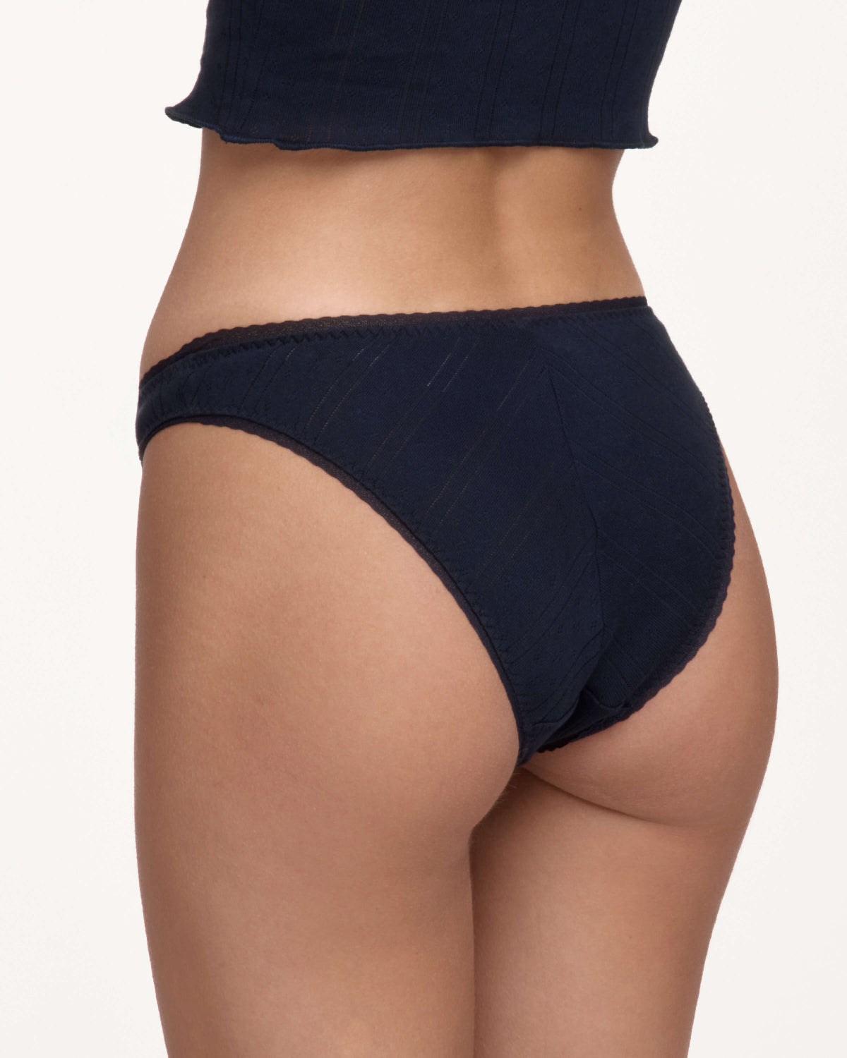 Rear view of a model wearing dark navy blue underwear against a plain off-white background.