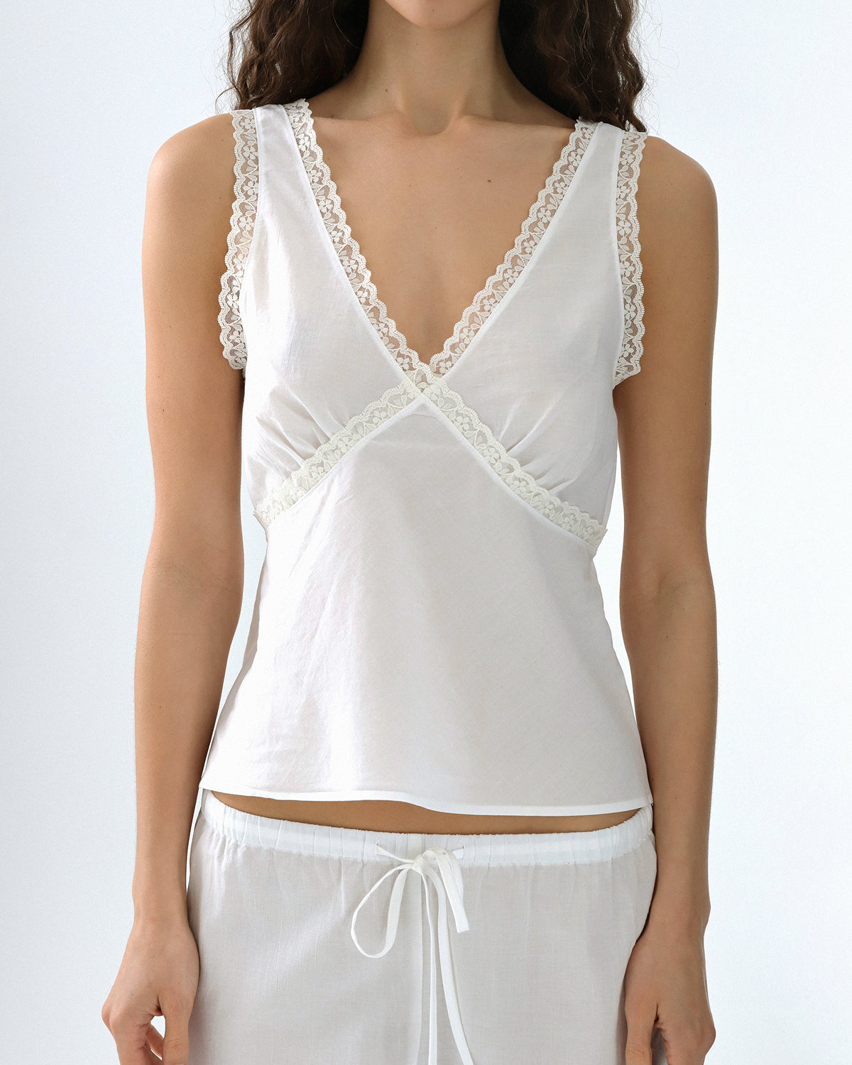 White lace-trimmed top worn by a person on a white background