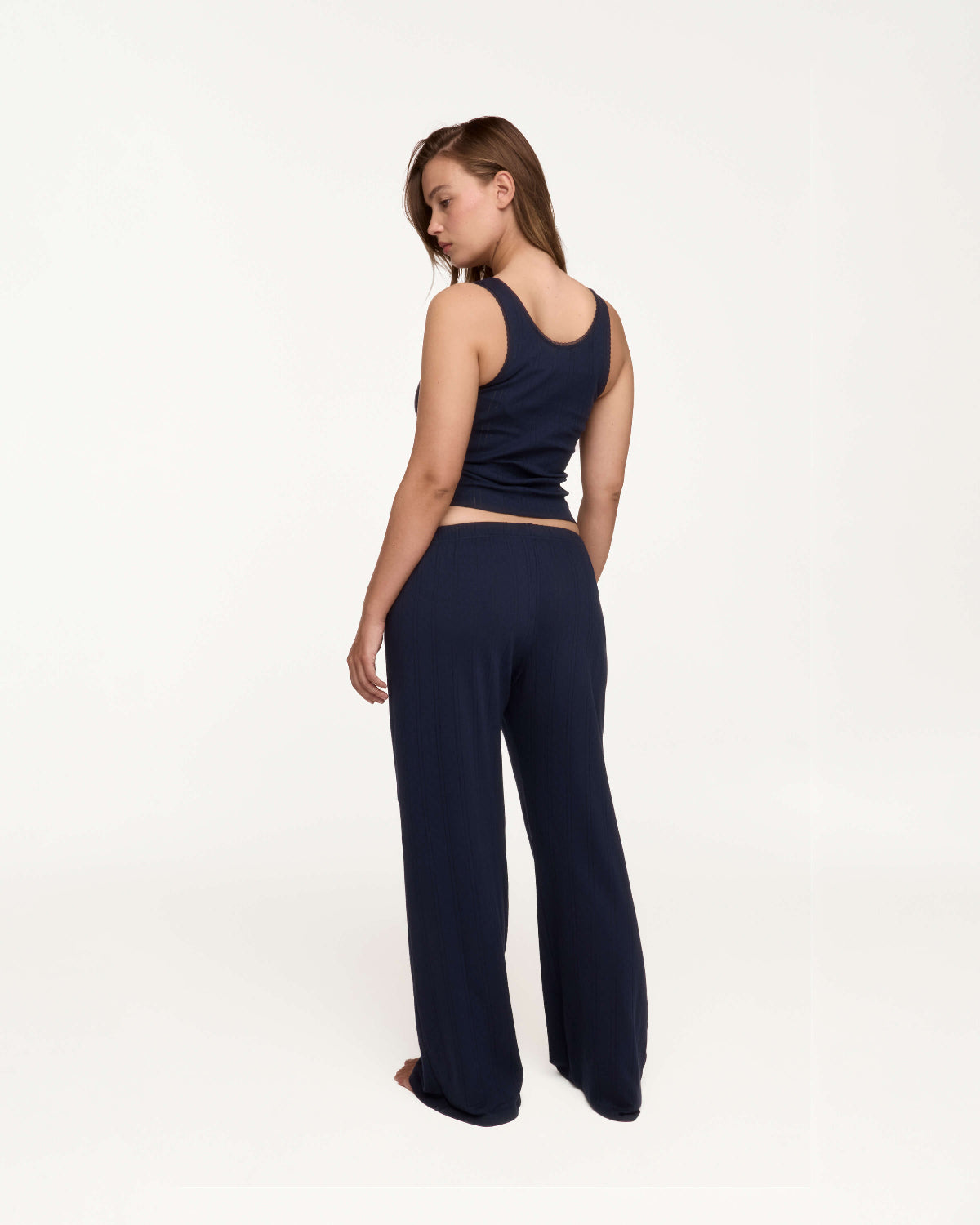 A woman modeling a matching navy blue loungewear set, featuring a cropped tank top and wide-leg pants, shown from a rear angle against a plain white studio background.