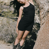 Woman in a black dress and boots standing against a desert backdrop