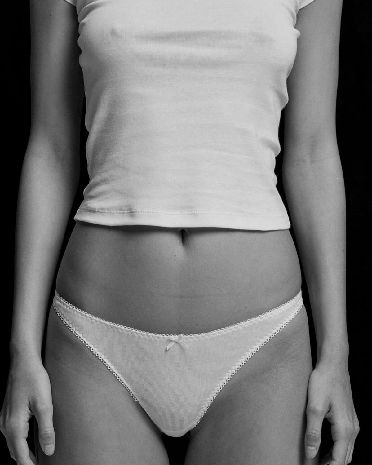 Person wearing a white t-shirt and light-colored underwear against a black background