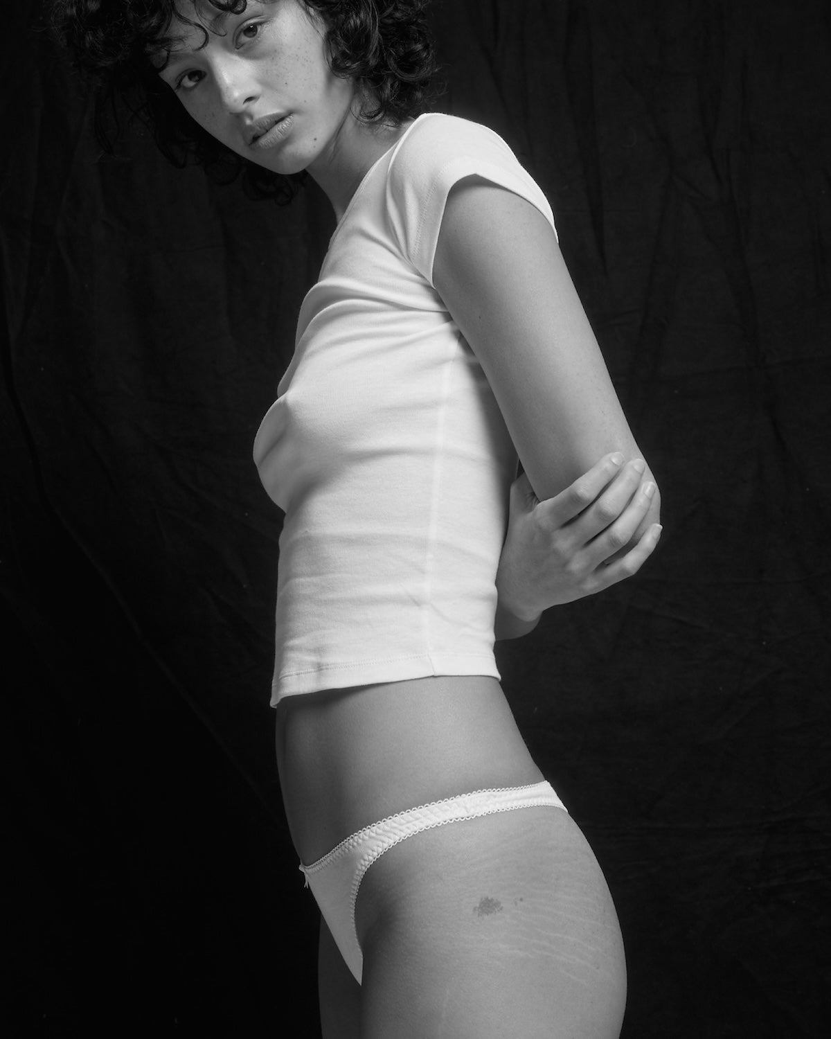 Person wearing a white t-shirt and underwear against a dark background