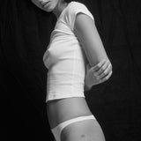 Person wearing a white t-shirt and underwear against a dark background