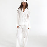 Woman wearing a white satin pajama set with a matching headband on a white background