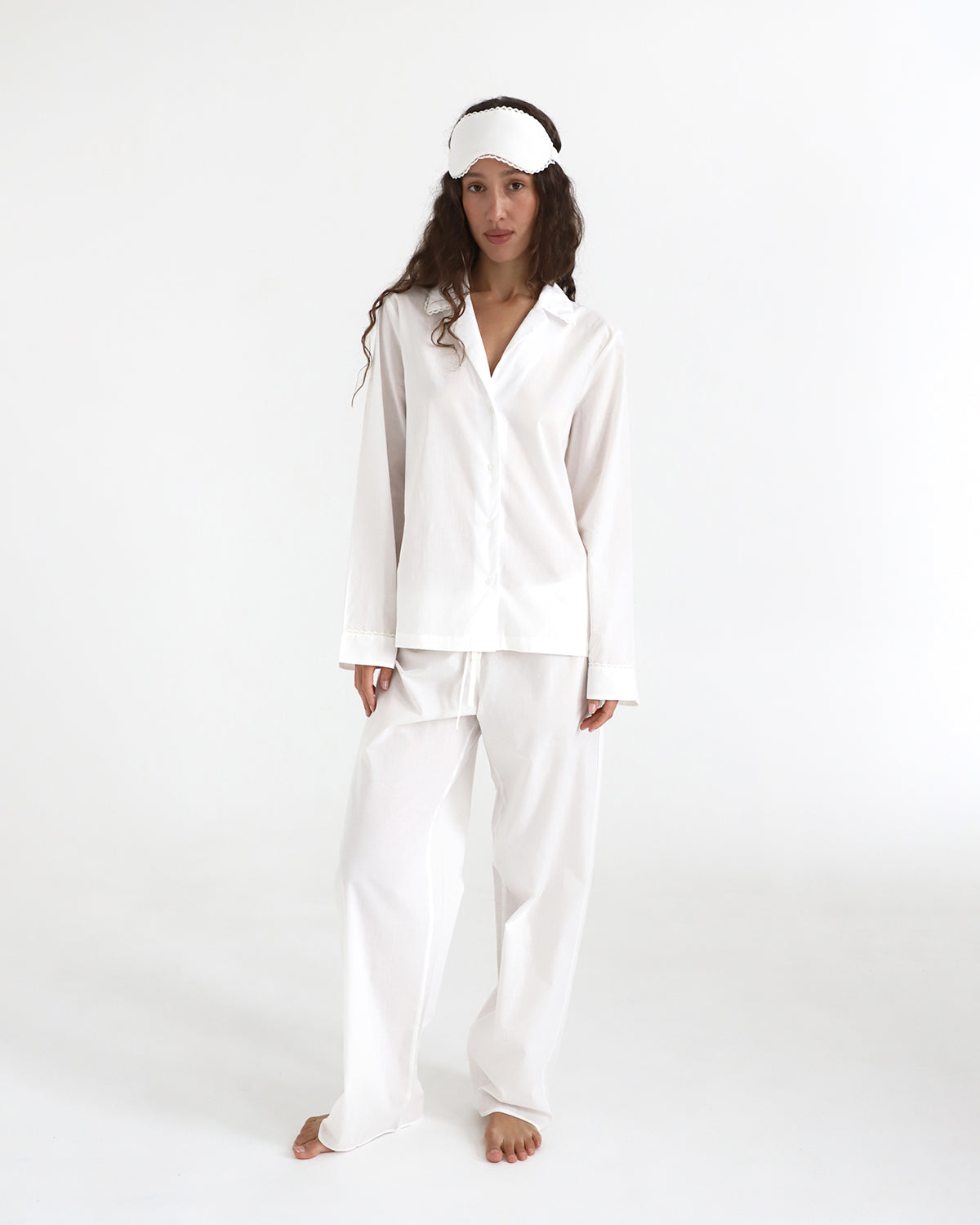 Woman wearing a white satin pajama set with a matching headband on a white background