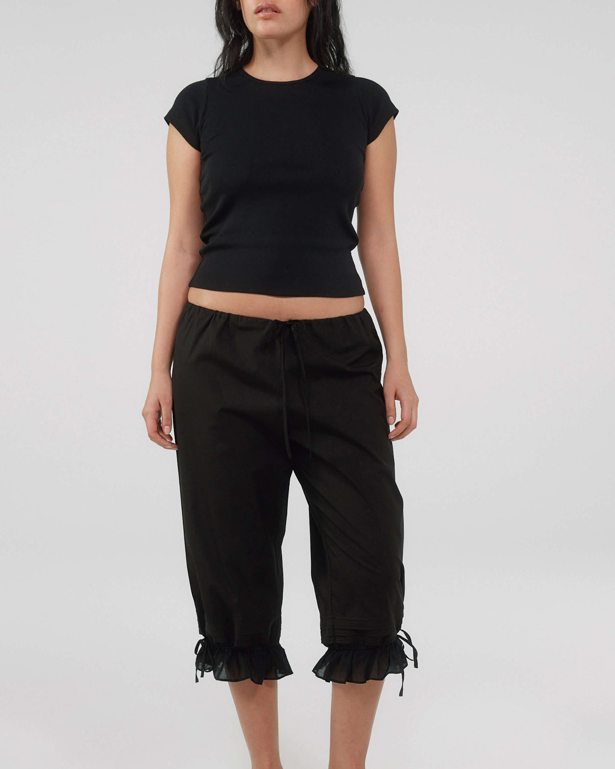 Person wearing a black crop top and black pants with ruffled hem on a white background