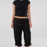 Person wearing a black crop top and black pants with ruffled hem on a white background