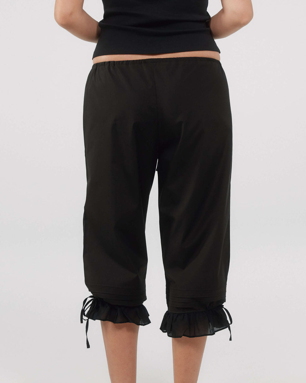 Person wearing black capri pants with ruffled cuffs on a white background