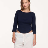 A woman modeling a navy blue long-sleeve boat-neck top, paired with white drawstring sweatpants, against a plain white studio background.