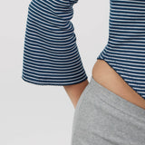Close-up of a person wearing a navy and white horizontally striped long-sleeve top with flared bell cuffs, paired with a light gray shorts.