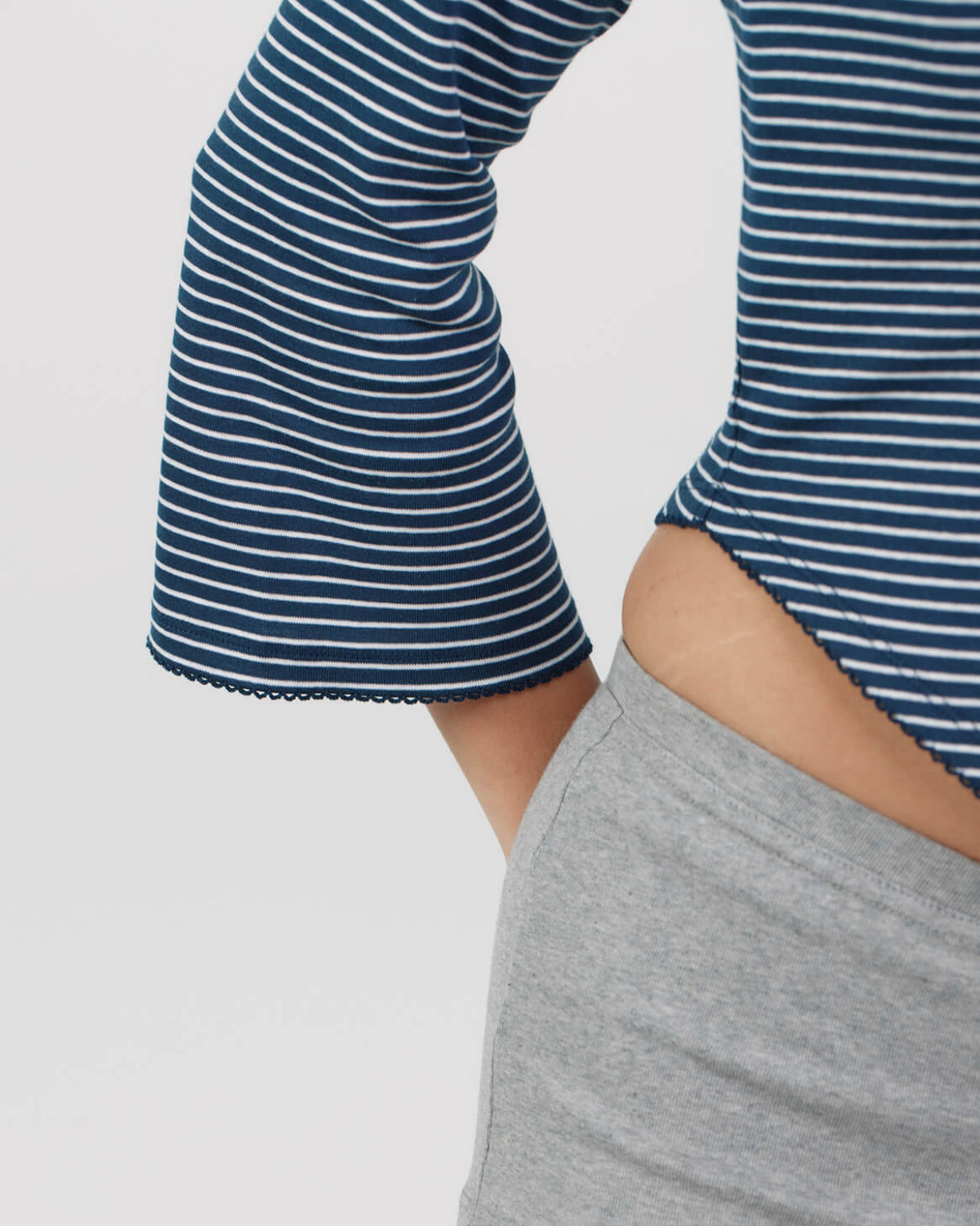 Close-up of a person wearing a navy and white horizontally striped long-sleeve top with flared bell cuffs, paired with a light gray shorts.