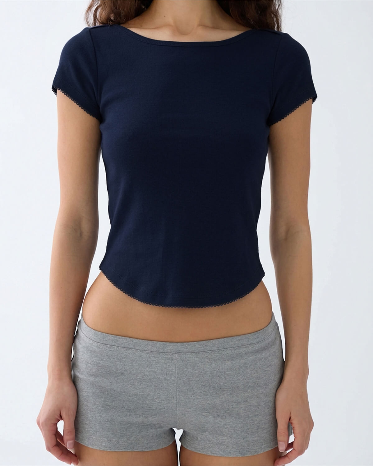 A woman wearing a navy blue short-sleeve knit top with scalloped edges and gray heather shorts, shown from the neck down against a plain light gray background.