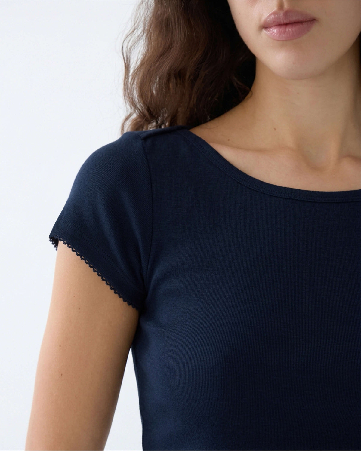 Close-up of a woman wearing a dark navy blue short-sleeve top with a boat neckline and delicate scalloped lace trim on the sleeve.