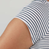 Close-up of a person wearing a white short-sleeve top with thin navy horizontal stripes and a scalloped lace-like hem.