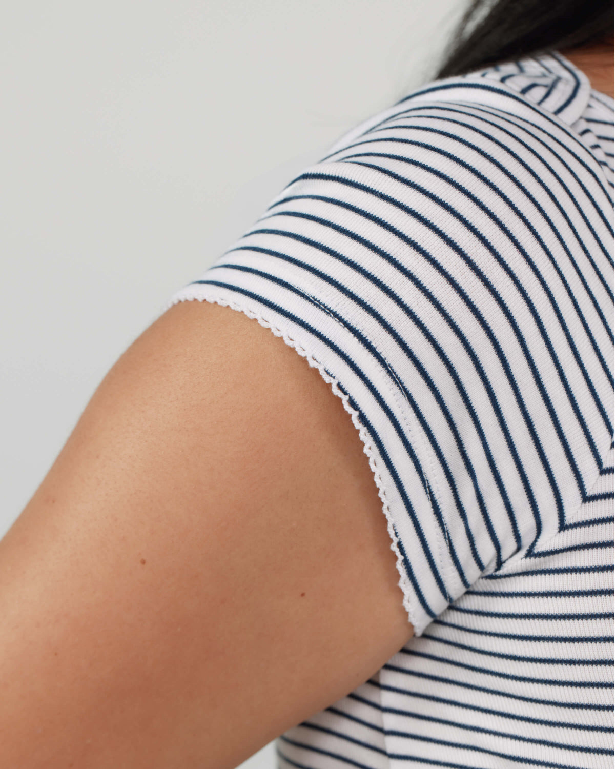 Close-up of a person wearing a white short-sleeve top with thin navy horizontal stripes and a scalloped lace-like hem.
