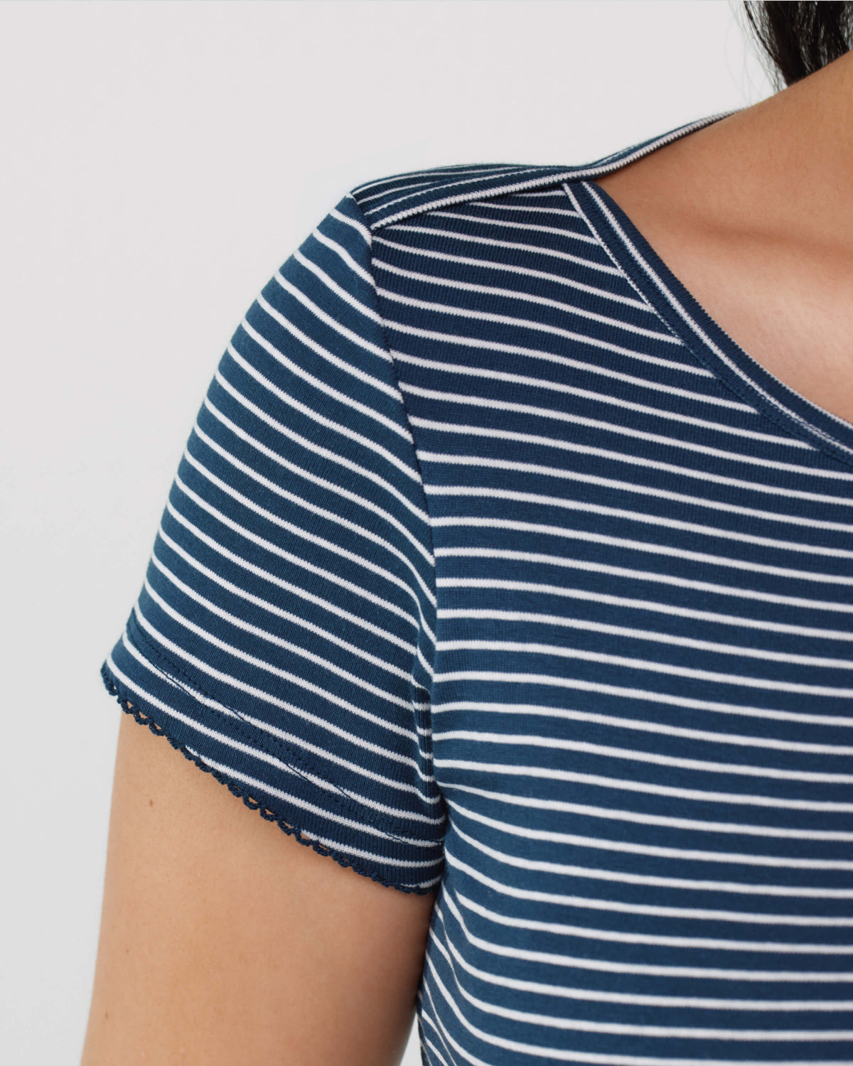 Close-up of a person wearing a short-sleeve top with navy blue and white horizontal stripes, showing the shoulder, sleeve, and side neckline against a plain light background.