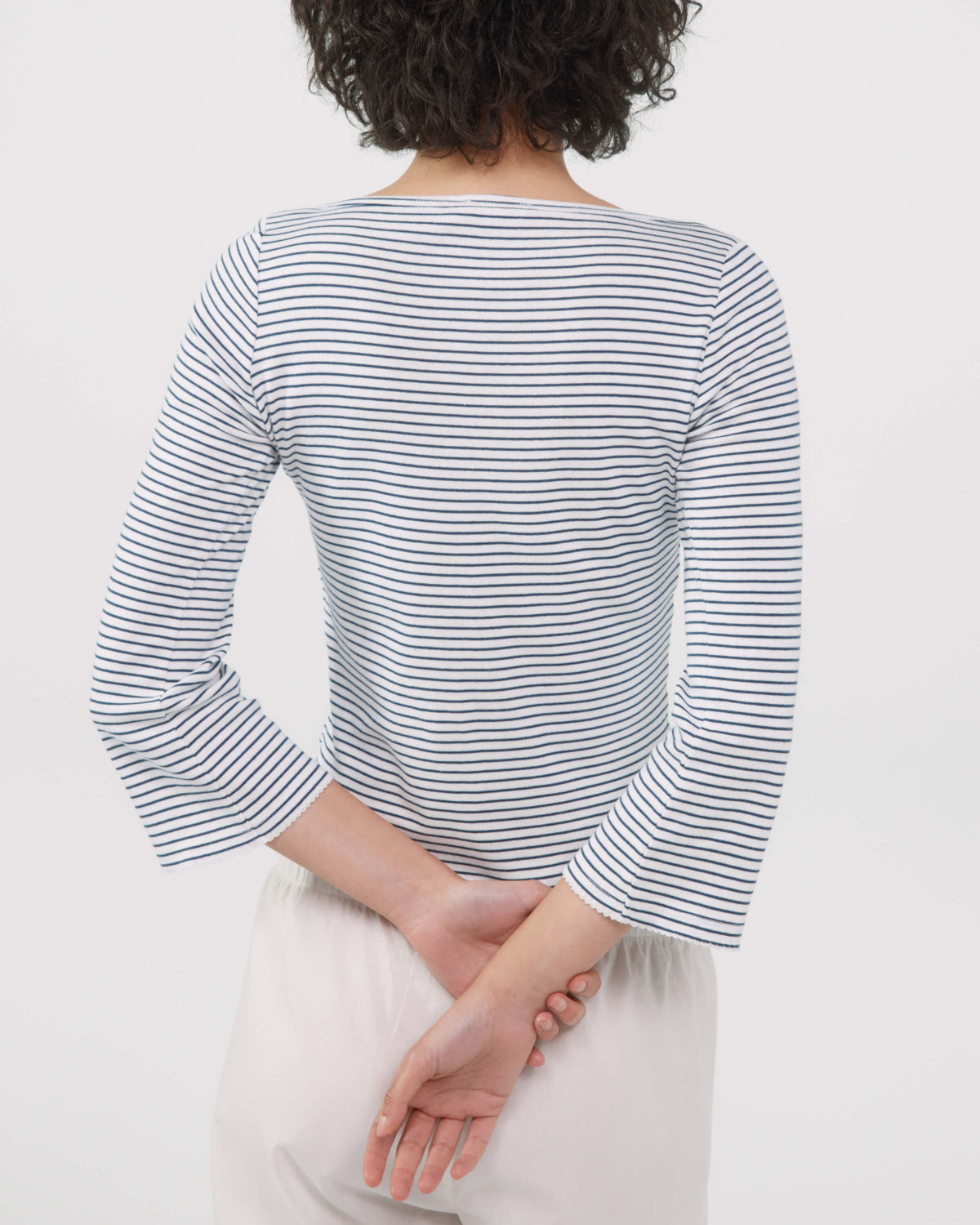 A person shown from the back wearing a long-sleeve top with thin navy and white horizontal stripes, paired with light-colored pants, against a plain light background.