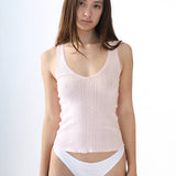 Woman wearing a light pink tank top and white underwear on a plain background