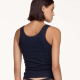 A woman shown from the back wearing a dark navy tank top with a lace-trimmed scoop neckline and matching low-rise thong bottoms, against a plain white studio background.