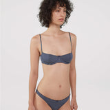 A model wearing a bra and thong with navy blue and white horizontal stripes, photographed against a solid light gray background.