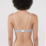 Rear view of a woman wearing a striped bra and thong with thin white straps and navy and white horizontal stripes, against a light gray studio background.