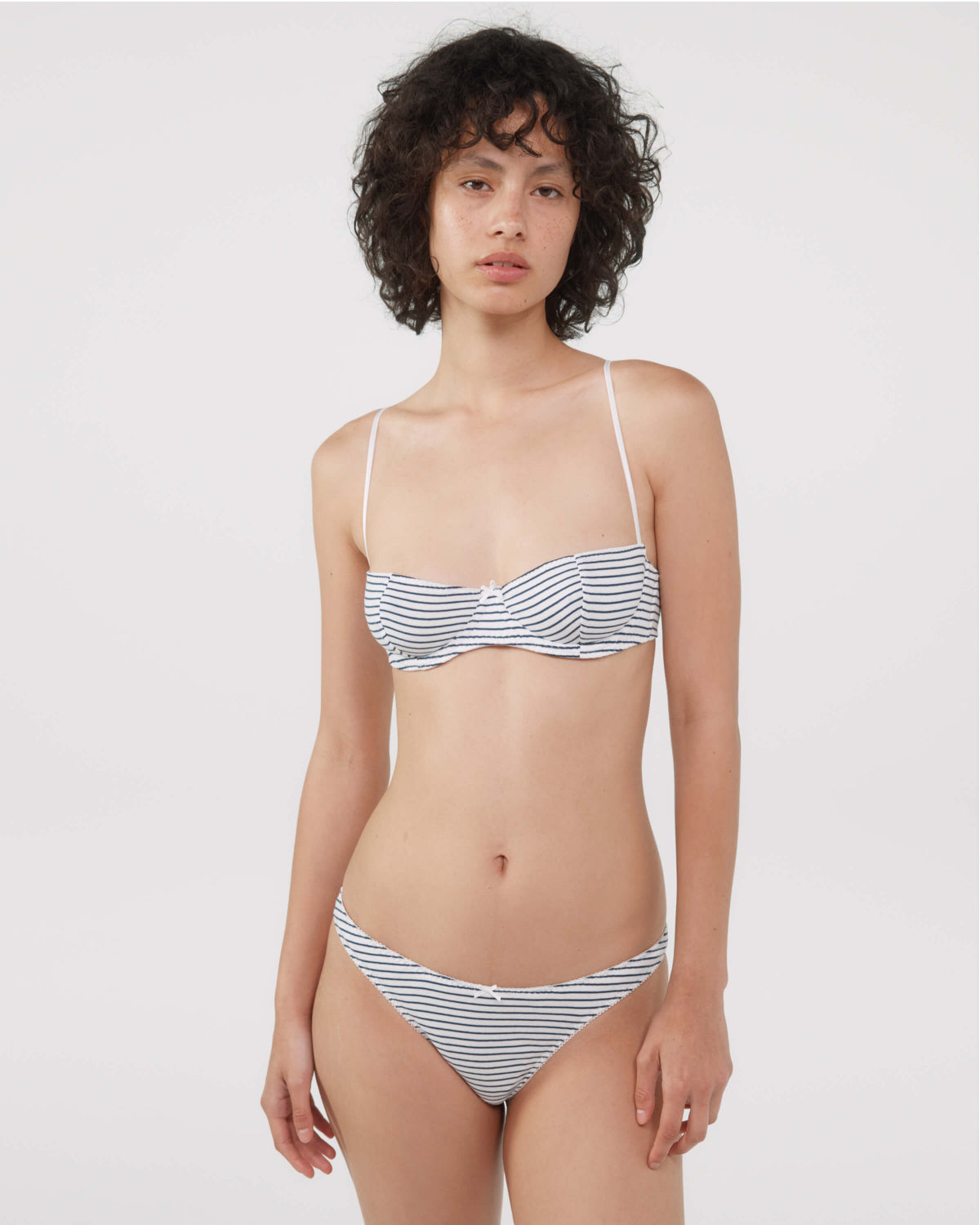A model wearing a bra and thong with a navy and white horizontal stripe pattern, photographed against a solid light gray background.