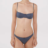 A model wearing a bra and thong with navy blue and white horizontal stripes, against a plain light gray background.