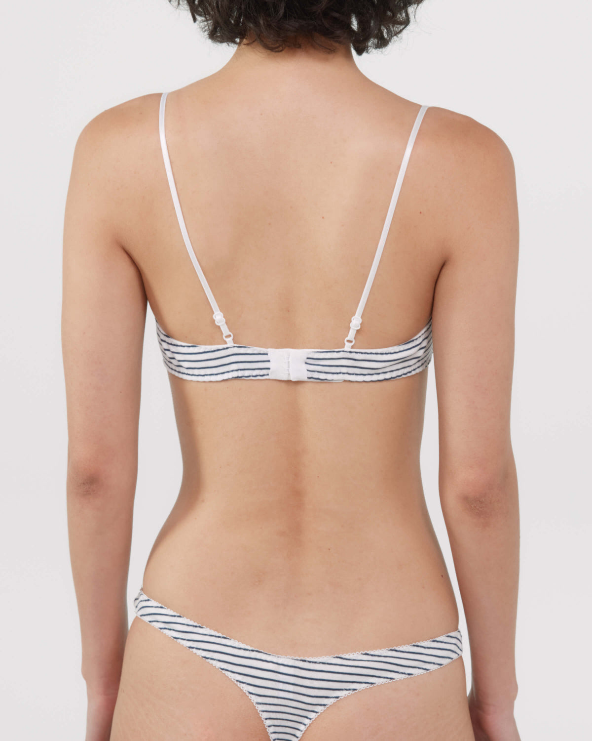 Rear view of a model wearing a bra and thong with thin navy and white horizontal stripes.