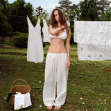 Woman in white outfit standing outdoors with laundry in the background
