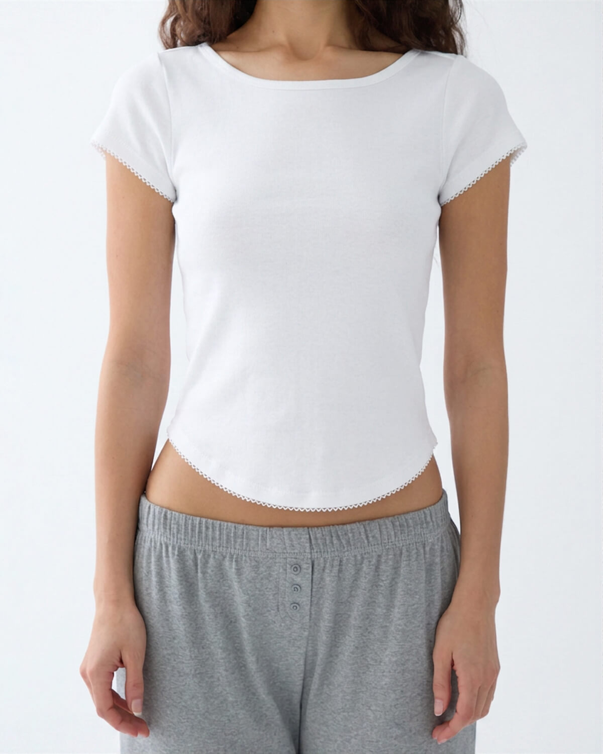 A woman wearing a white short-sleeve crop top with scalloped edges and gray heathered lounge pants, shown from the neck down against a plain white background.