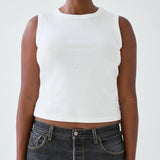 Person wearing a white sleeveless top and dark jeans on a plain background